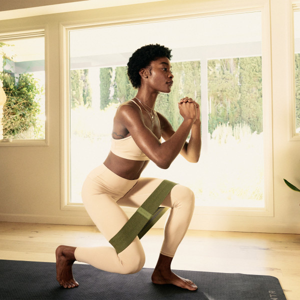 Person performing resistance band lunges indoors with a fabric resistance band from the Centr Fitness Kit around their thighs.