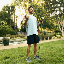 Person performing standing bicep curls outdoors using tube resistance bands from the Centr Fitness Kit.