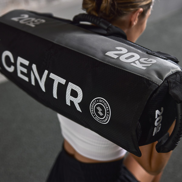 Lifestyle image of the CENTRxHYROX 20kg Competition Sandbag. The image is looking down at the model who has the sandbag on their shoulders. The image focuses on the "Official Competition Equipment" Stamp.