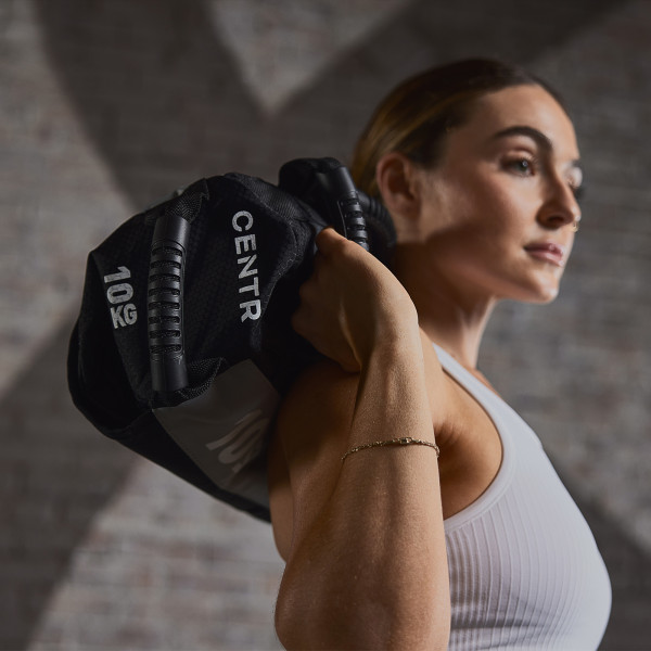 Lifestyle image of the CENTRxHYROX 20kg Competition Sandbag. The image is looking up at the model who has the sandbag on their shoulders. The image focuses on the side of the bag.