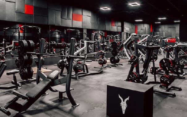Multiple fitness equipment standing in a gym with black floor, walls and ceiling.
