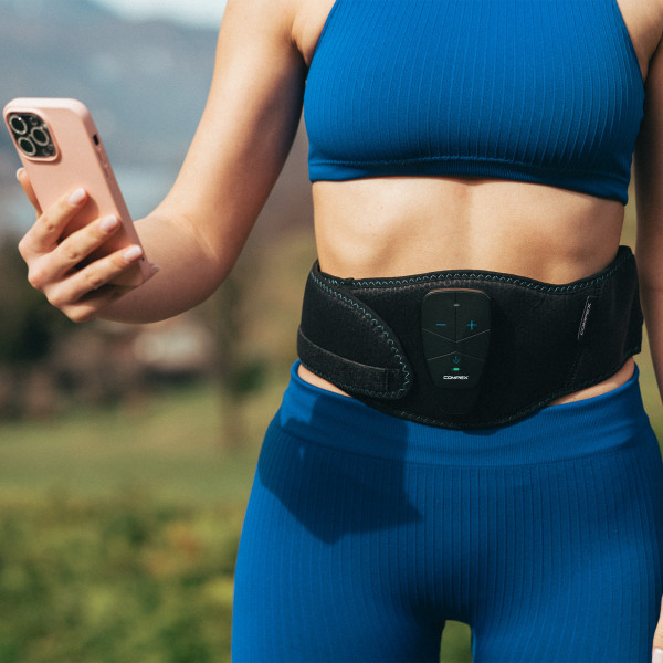 Lifestyle image of the compex core belt 5.0 - model is wearing the belt and using their phone