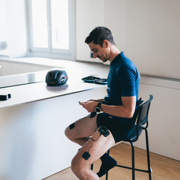 Lifestyle image of the Compex MINI TENS Muscle Stimulator - Model sitting and using the stimulator on their legs