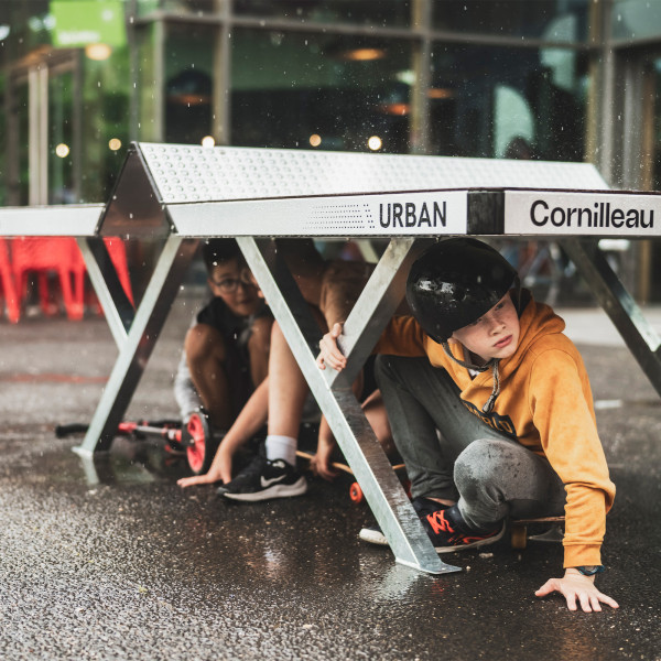 Children sheltering under the Cornilleau Urban Outdoor Table Tennis Table in the rain