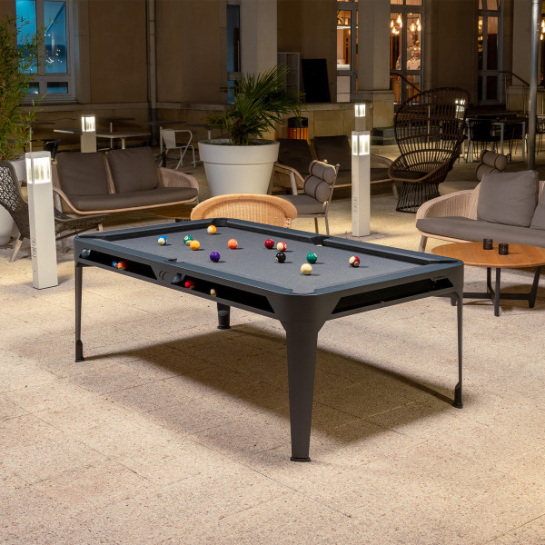 Outdoor view of the Cornilleau Play-Style Hyphen pool table with black frame and light grey cloth by a hotel terrace
