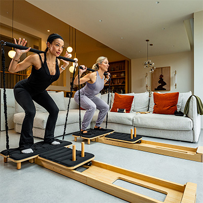 Models performing squats with the Gymproluxe Portable Pilates Reformer  