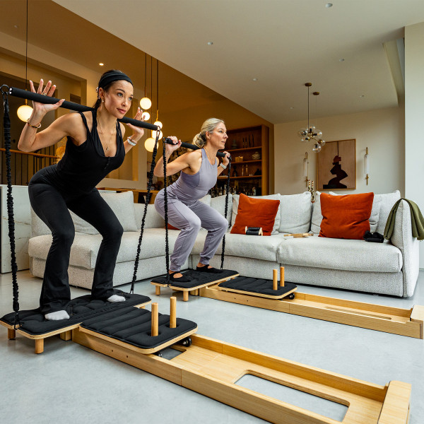 Models performing squats with the Gymproluxe Portable Pilates Reformer