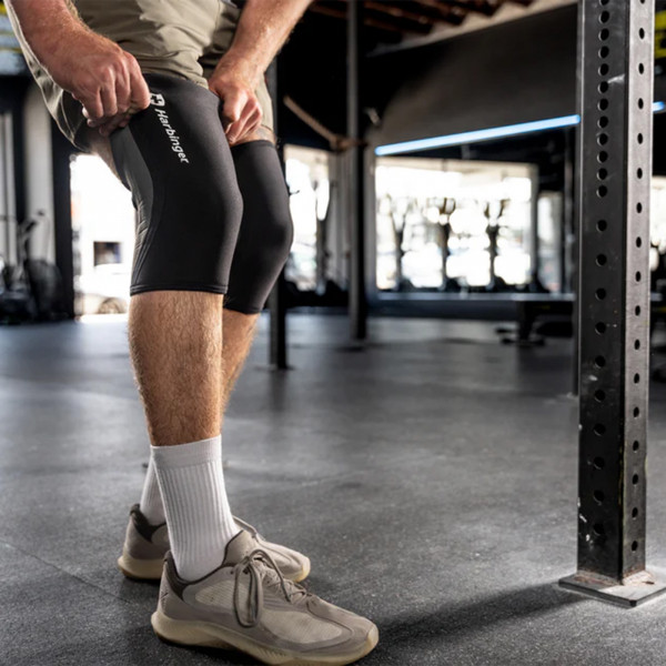 A lifestyle image of a model pulling up Harbinger Pro 7mm Knee Sleeves over their knee