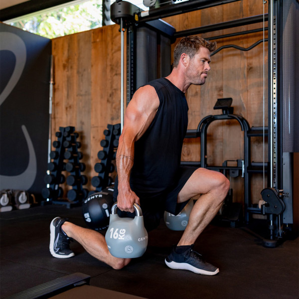 Chris Hemsworth doing a weighted lunge with kettlebells in front of the Inspire Fitness FT2 PRO Functional Trainer.
