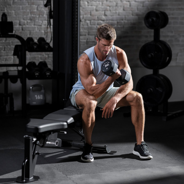 Lifestyle image of the Inspire Fitness FID7 Bench. A model is using dumbbells to perform bicep curls