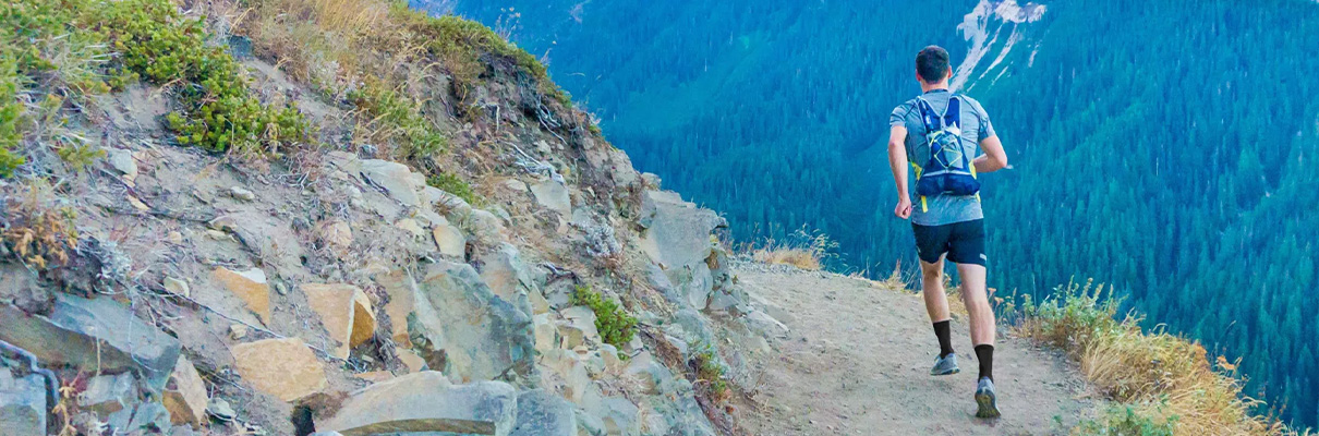 Model trail running along a rocky mountain path with forested hills in the background