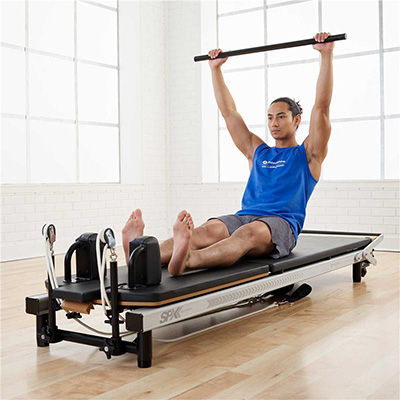 Model performing an overhead press on the Merrithew At Home SPX Reformer Package With Vertical Stand  