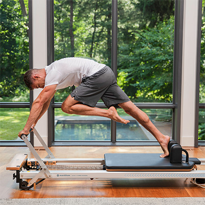 Model performing a plank variation on the Merrithew At Home SPX Reformer Package With Vertical Stand