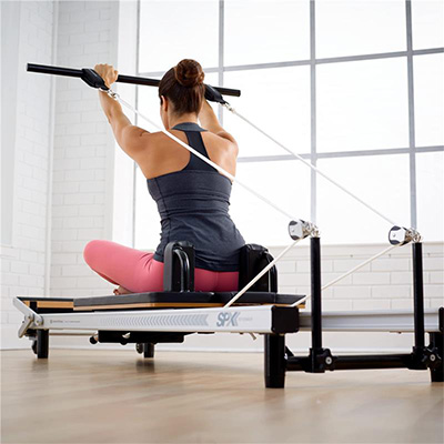 Model performing a seated lat pulldown on the Merrithew At Home SPX Reformer Package With Vertical Stand  