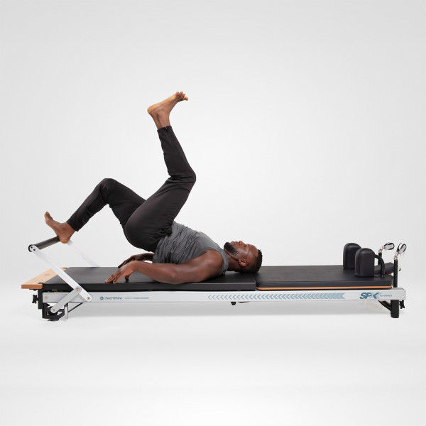 Model performing a shoulder bridge on the Merrithew At Home SPX Reformer Package With Vertical Stand