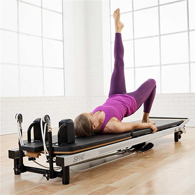 Model performing a single leg bridge on the Merrithew At Home SPX Reformer Package With Vertical Stand  