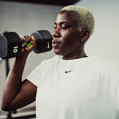 Person performing a standing curl using a Nike Strength Black Dumbbell during an indoor gym workout. 