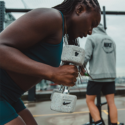 Person training outdoors using a Nike Strength Grind Dumbbell during a bent-over row exercise.