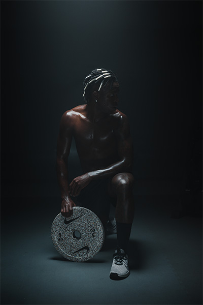Model kneeling with a Nike Strength Grind Bumper Plate