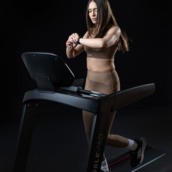 Model adjusting a smartwatch on the NoblePro Elite E8s Treadmill
