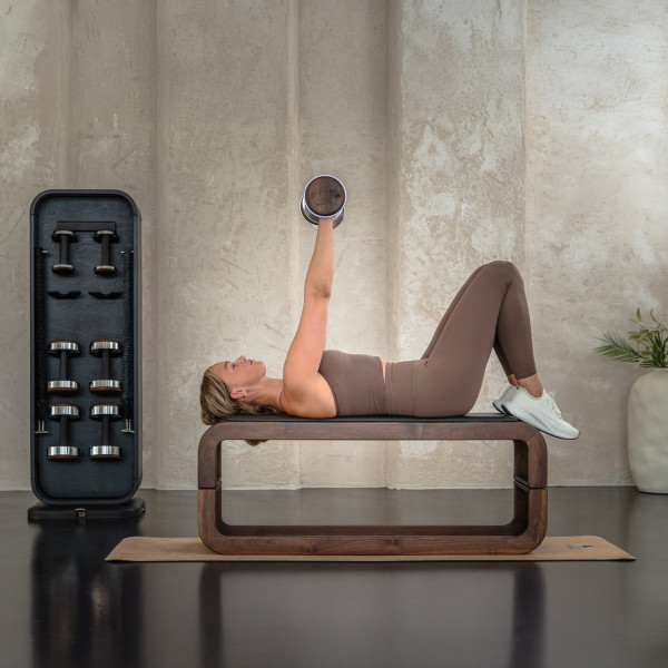 Person performing dumbbell press on bench with NOHRD StepTower nearby