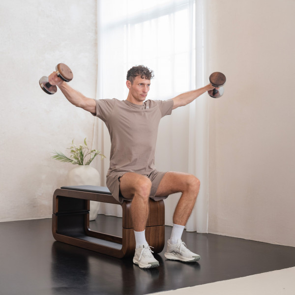 Person seated on bench performing dumbbell lateral raise