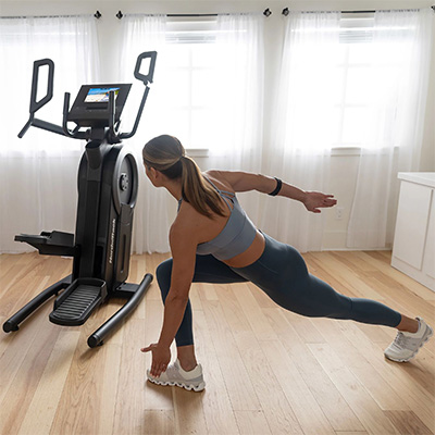 Wide view of a user performing a lateral lunge stretch beside the NordicTrack Step Climber 
