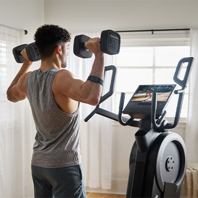 Rear view of a user performing dumbbell shoulder press beside the NordicTrack Step Climber XL 