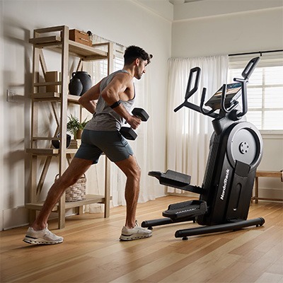 Side angled view of a user performing weighted step training with dumbbells beside the NordicTrack Step Climber XL 
