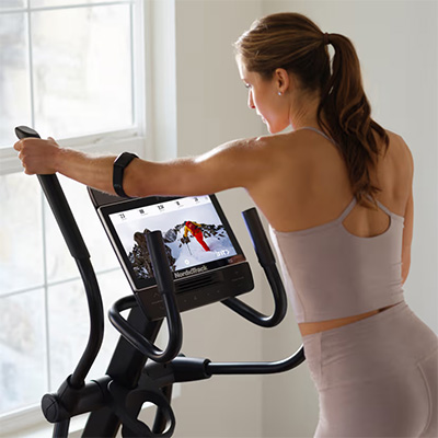 Close-up of a model holding the handles of the NordicTrack AirGlide 14i Elliptical with the display screen visible 