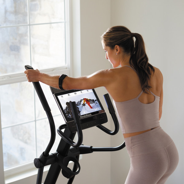 Close-up of a model holding the handles of the NordicTrack AirGlide 14i Elliptical with the display screen visible