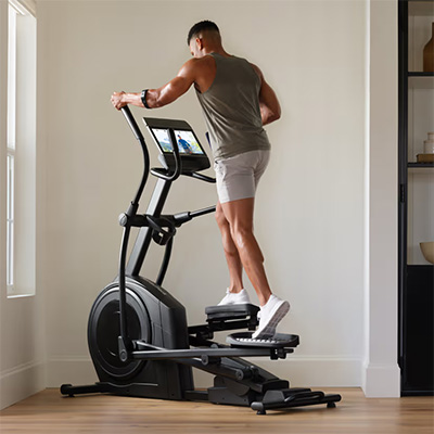 Person training on the NordicTrack AirGlide 14i Elliptical from a rear angle in a home space 