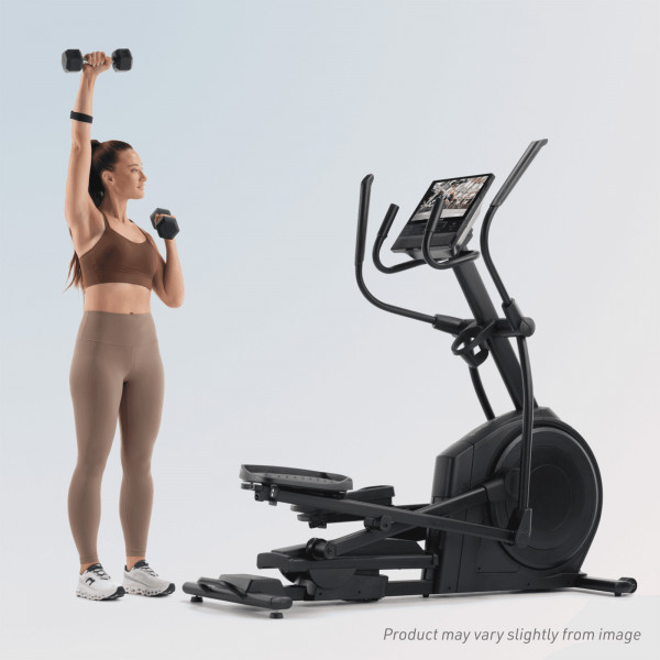 Model performing a dumbbell shoulder press beside the NordicTrack AirGlide 16 Elliptical