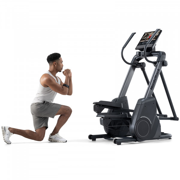 Person doing exercises next to the NordicTrack X16 Elliptical Cross Trainer with a workout displayed on the screen.
