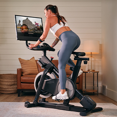 Rear angled view of a model cycling on the NordicTrack X24 Bike with workout displayed on screen 