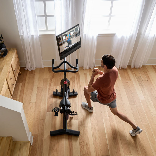 Top view of NordicTrack 24 Studio Exercise Bike with model performing forward lunges beside it