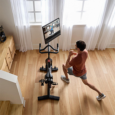Person doing a lunge exercise beside the NordicTrack S24 Studio Bike screen