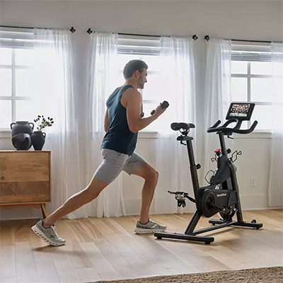 User doing dumbbell lunge workout beside the NordicTrack T Series 9 Bike