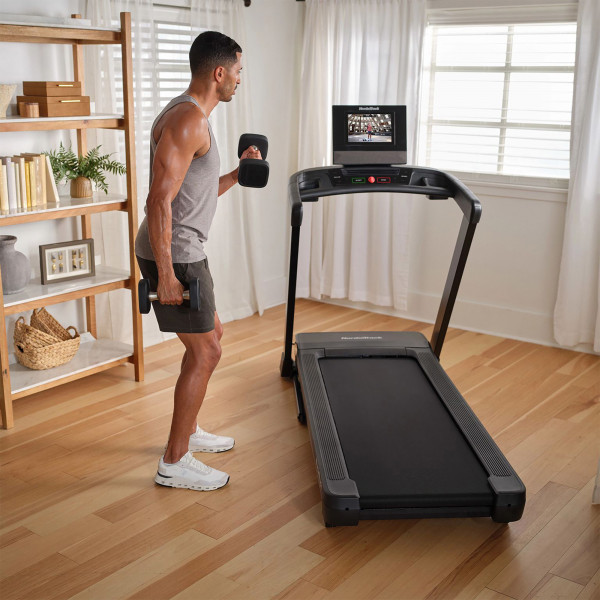 Model performing bicep curls next to NordicTrack T Series 10 Treadmill in home setting