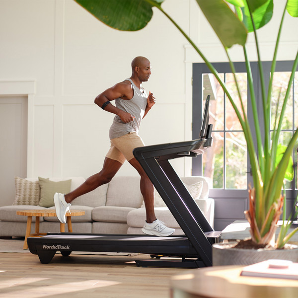Right side view of a person running on the NordicTrack Commercial 2450 Treadmill with iFIT workout displayed.