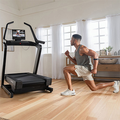 Model performing lunges next to the NordicTrack X16 Treadmill in a home setting 