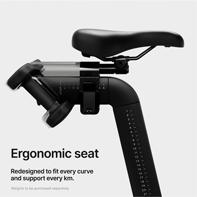 An infographic stating: "Ergonomic seat. Redesigned to fit every curve and support every km." A subtitle states: "Weights to be purchased separately," referencing the image, which shows two Peloton dumbbells in the dumbbell cradle behind the seat. The Peloton Dumbbells are available for purchase at Fitshop.