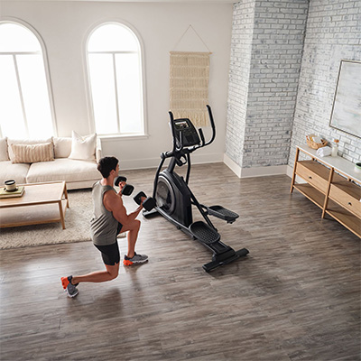 Person exercising with dumbbells next to the ProForm Carbon E7 Elliptical