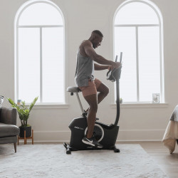 Lifestyle image of the ProForm 225 CSX Upright Exercise Bike showing a model riding the bike from the side in a home setting