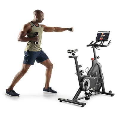 Model doing dumbbell lateral raise next to the ProForm Sport CX Bike