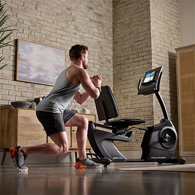 Wide view of a user performing a reverse lunge beside the ProForm 325 CSX Recumbent Bike 