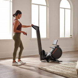 Lifestyle image of the ProForm 550R Rower in a home setting. The model is folding the rower.