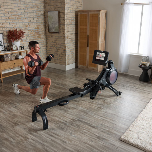 Model performing a dumbbell lunge beside the ProForm Carbon Pro10 Rower