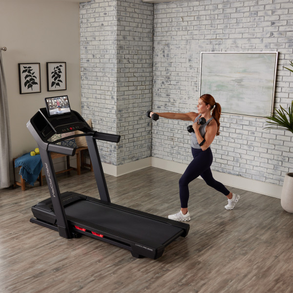 Model doing dumbbell lunges beside the ProForm Carbon Pro 9000 Treadmill