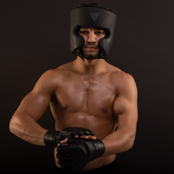 An image of a male-bodied model wearing the RDX Head Guard whilst adjusting the matching RDX Noir MMA Gloves.